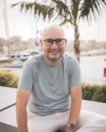 Florian sitting on a bench at a marina, smiling into the camera
